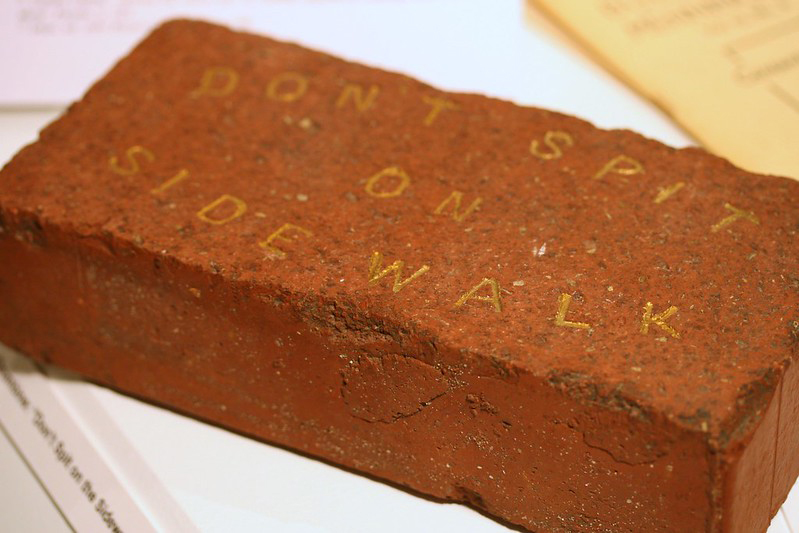 A red clay brick with the words "Dont Spit on Sidewalk" engraved across the top